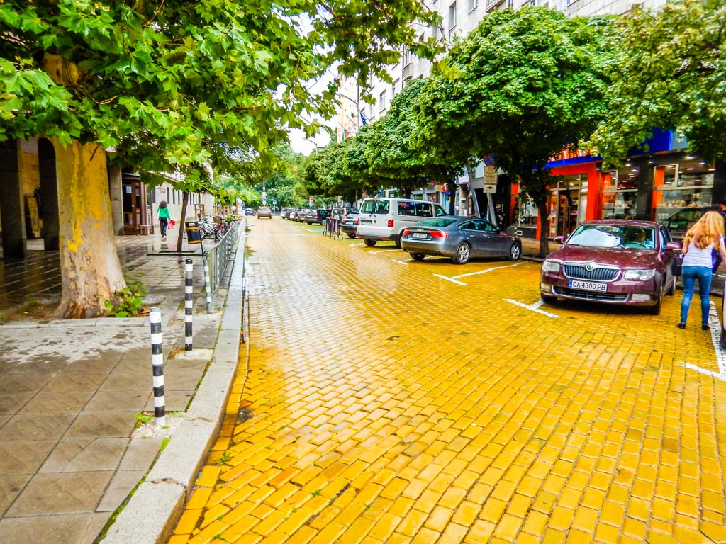 A city street with yellow bricks and some locals walking.