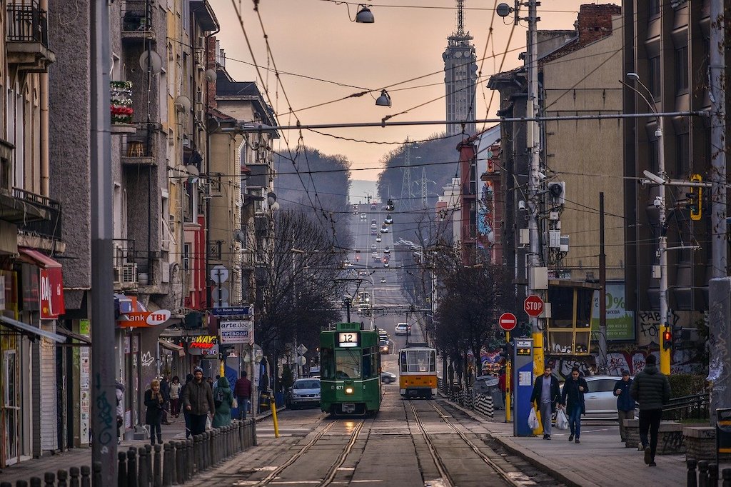 A narrow street during sunset with locals walking and a public tram.